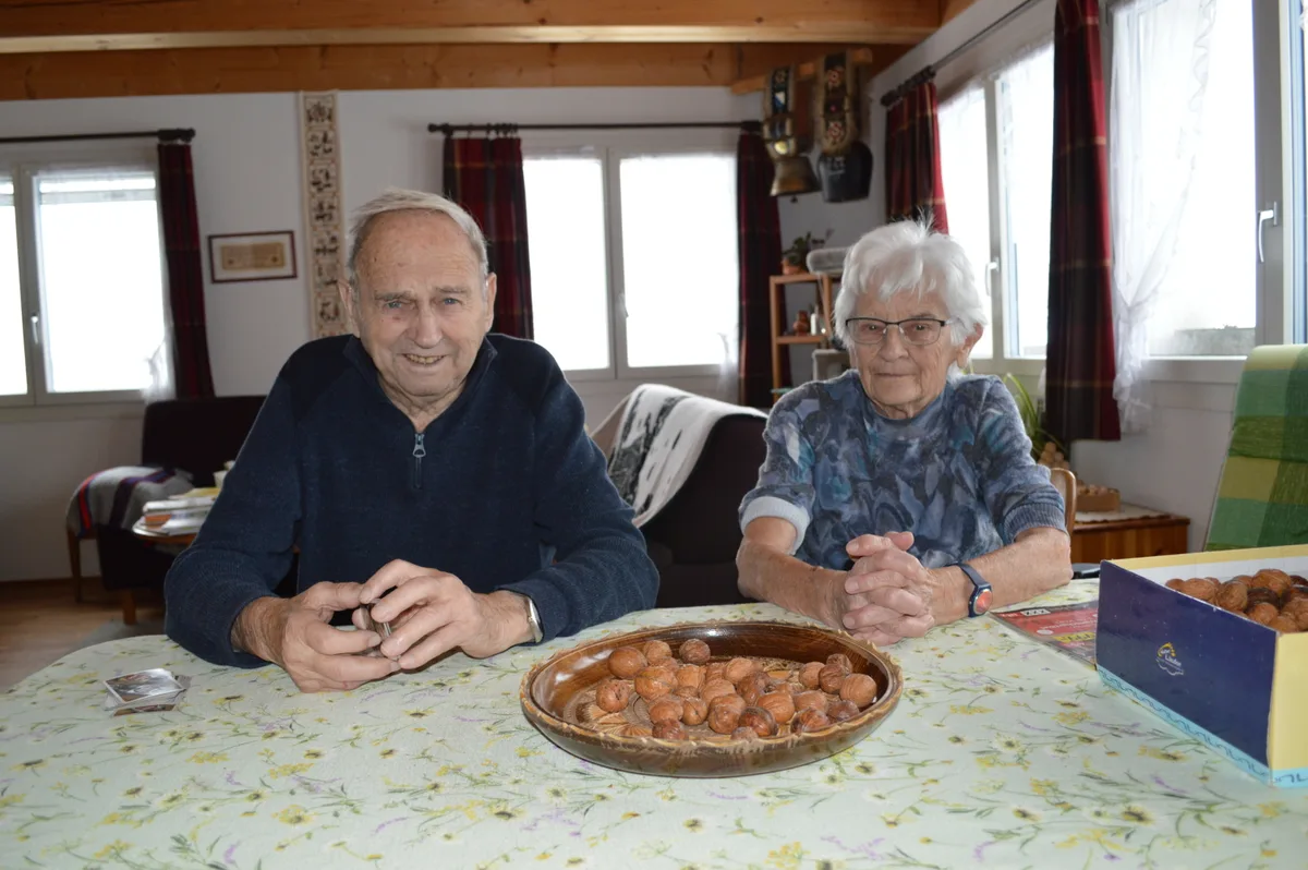 Ein Mann und eine Frau sitzen am Tisch, haben unzählige Baumnüsse und spielen darum.